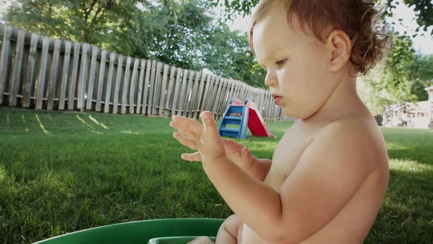 A young baby is sitting in a pool outdoors in the day time