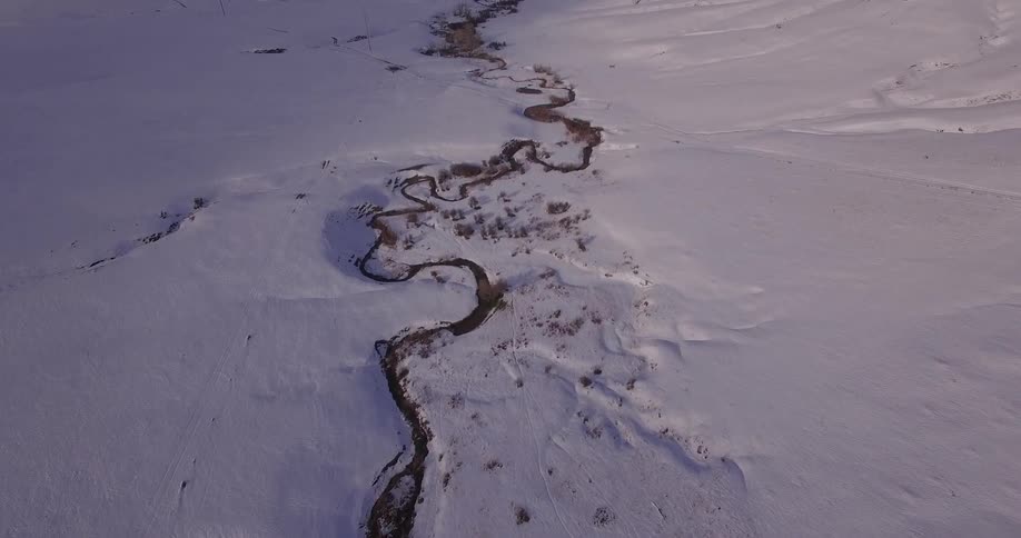 Top down aerial view of a winding river flowing through the plains covered in snow