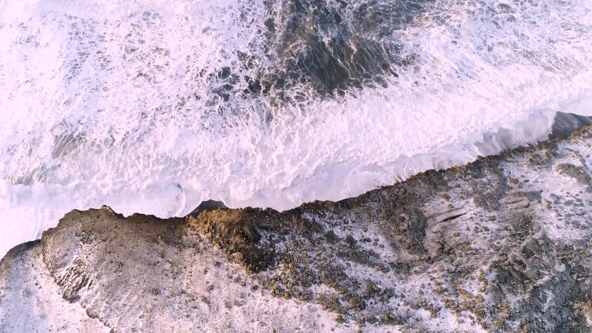 Ocean waves crashing against an coastline cliff and rolling back into the ocean
