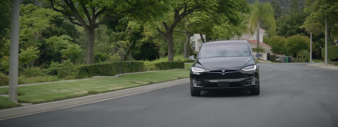 A black luxury sedan drives on the streets of a suburb at morning