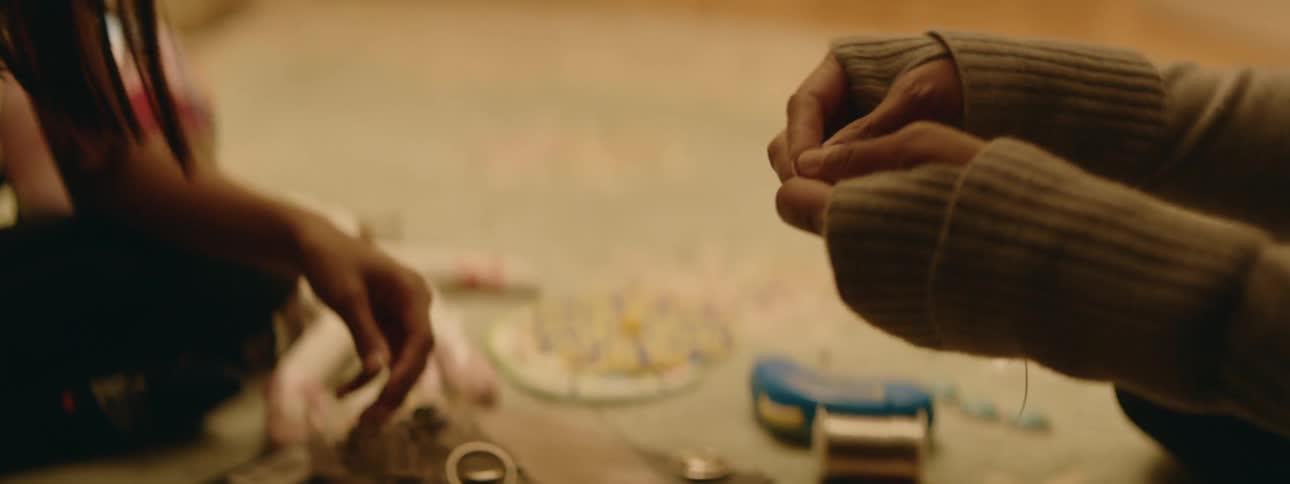 A close up of a young girl sitting on the floor putting jewelry together with an adult