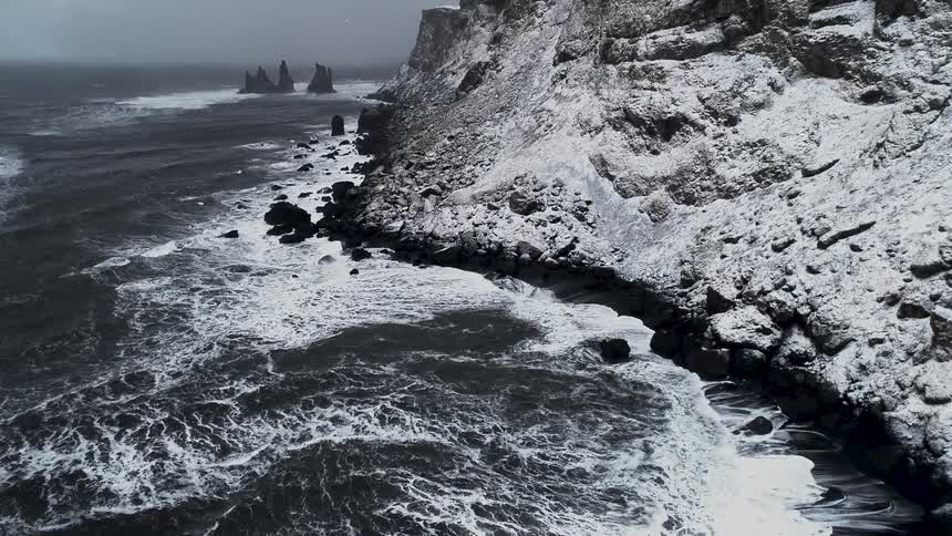 A view of sea waves washing up against rocky snowcovered cliffs