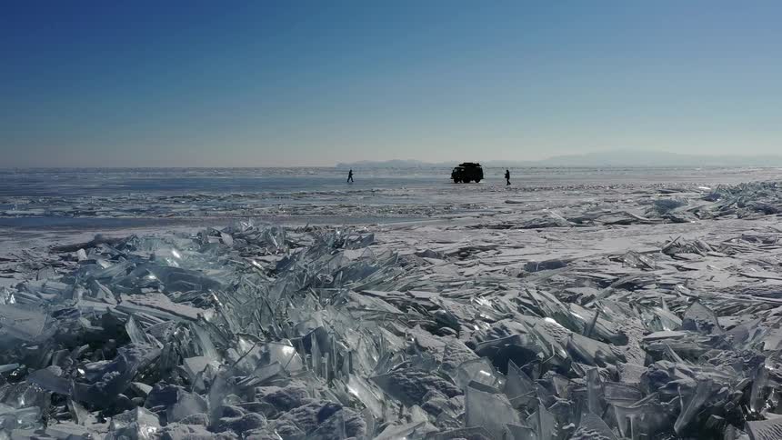 Silhouette of two people walking around a vehicle parked on an ice field at day time
