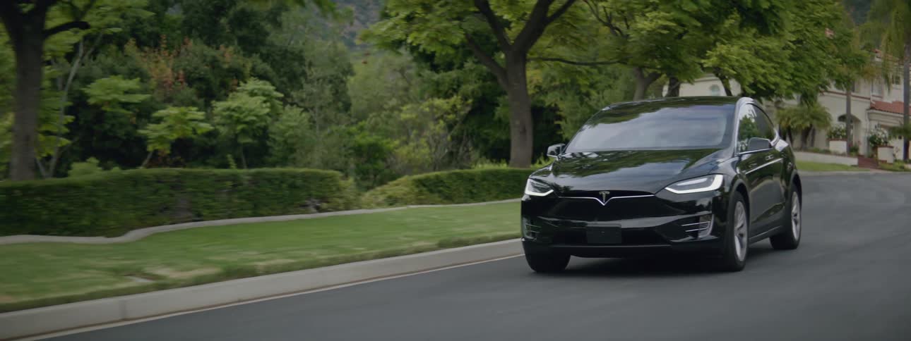 A black luxury sedan drives on the streets of a suburb at morning