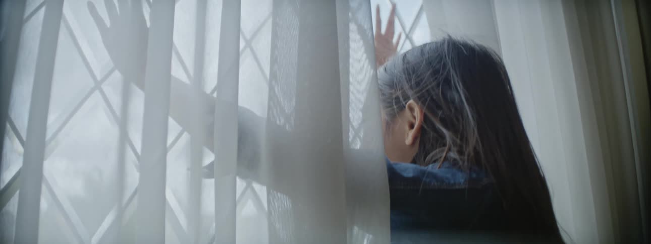 A young girl standing at a window with her arms spread and her hands pressed against it