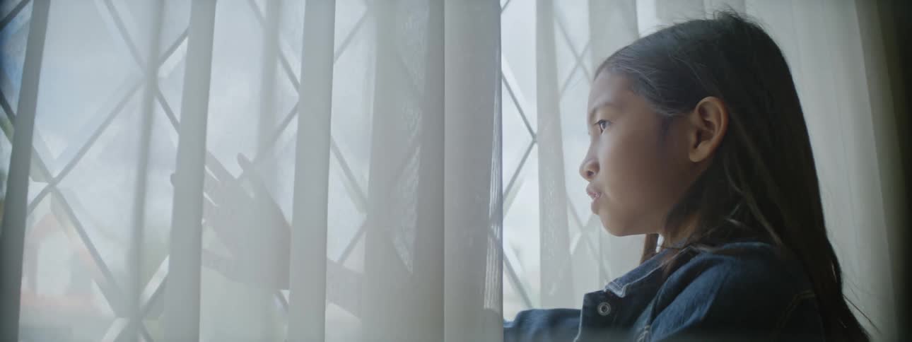 Young kid is indoors and looking outside the window