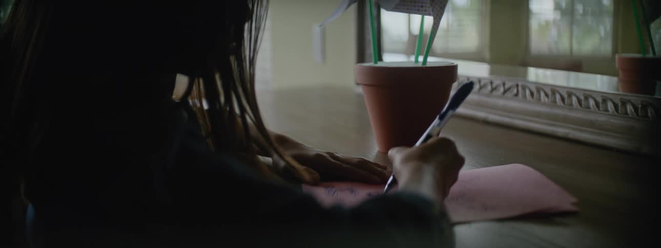 A young kid is indoors and writing on a piece of paper
