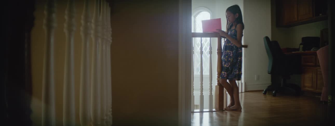 Girl stands at rail on upper floor in home reading paper