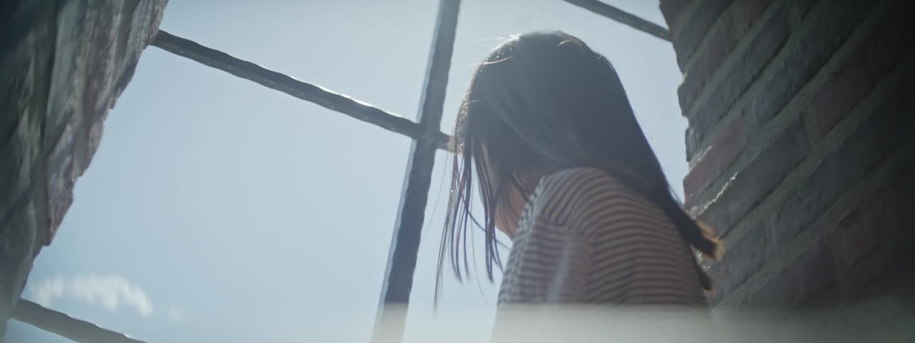 Back of a girl with long hair looking out of a window at daytime