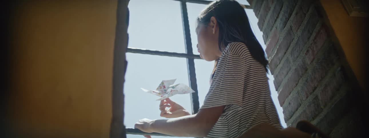 Girl sits in window nook blowing to spin pinwheel