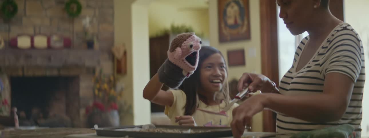 A mother and daughter stand next to each other at the counter as the mother takes cookies off the pan