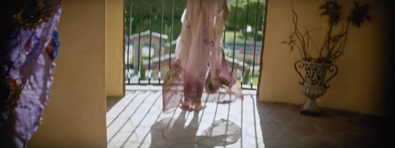 Girl opens her arms to extend a colorful translucent gauze cape in the balcony under the sun