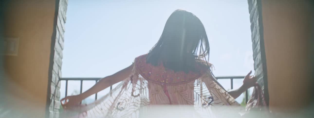 Girl opens her arms to extend a colorful translucent gauze cape in the balcony under the sun