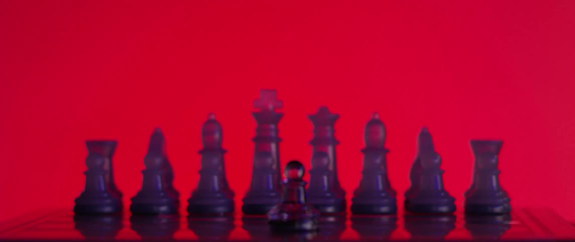 Rack focus of purple plexiglass or semiclear resin chess pieces on board against a background lit with red light