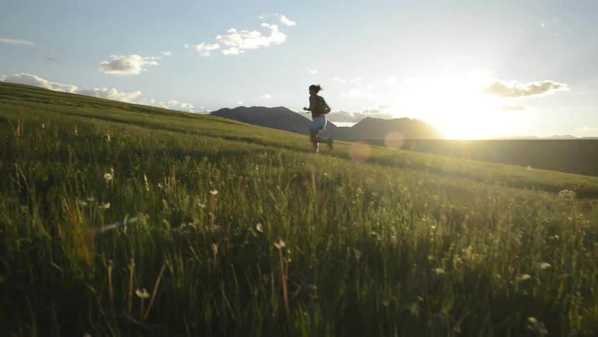A woman jogs along a dirt trail along a grassy plain with background hills in the day