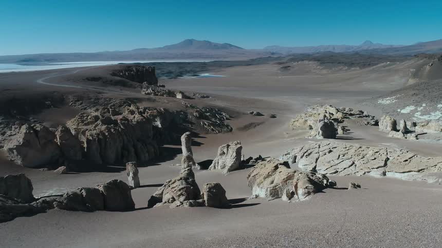 An aerial of a sand dune in the desert with rock formations and mountains in the distance