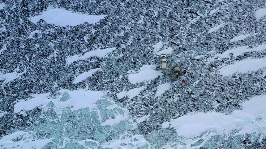 Top down aerial view of people around cars parked on the coast of a frozen lake