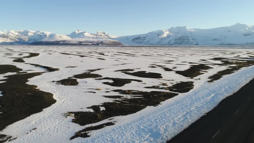Aerial view of a road through the plains covered in snow next to the mountains at daytime