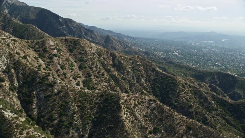 Aerial view of mountain ridges in La Crescenta California with scattered plants and trees under a hazy sky