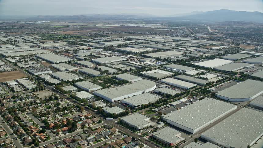 Aerial footage flying over homes and Don Antonio High School approaching warehouses in Chino California