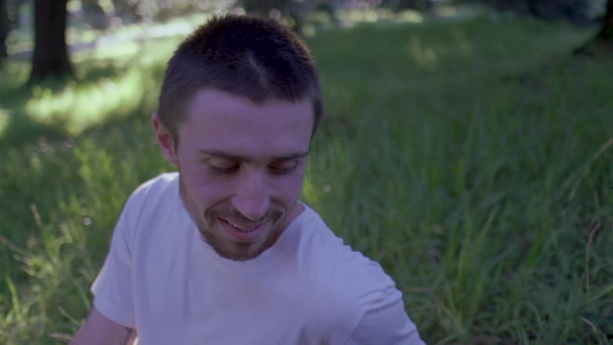 Man with another person sitting in the grass smiling and enjoying the day maybe a picnic maybe romantic