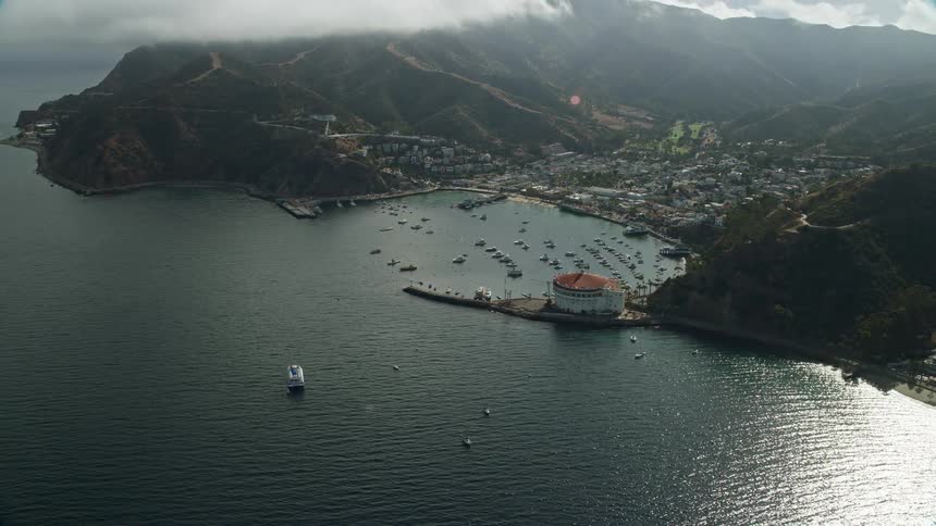 Aerial footage of Avalon Catalina Island California showing a reverse view of the harbor and coastal town with boats docked in the marina