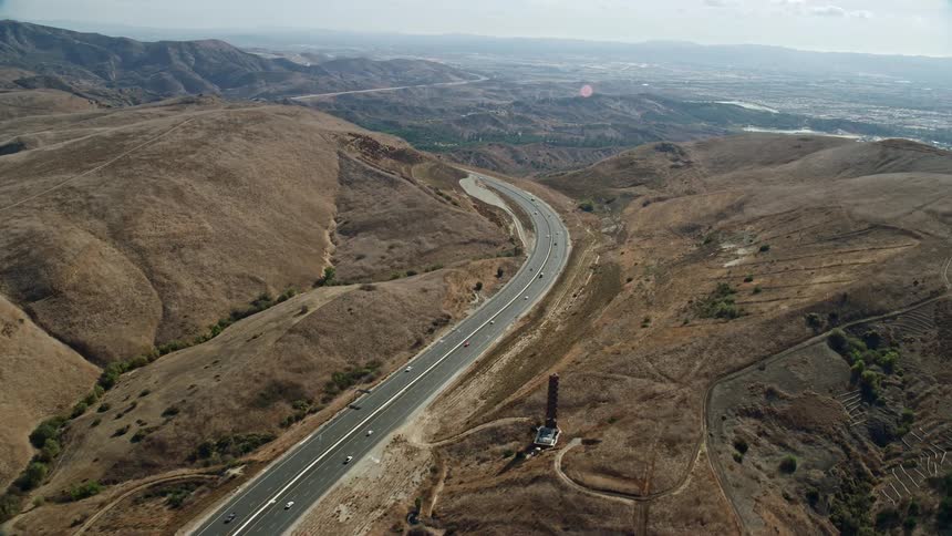Aerial footage captures light traffic on a freeway weaving through hills in Irvine California during a partly cloudy day