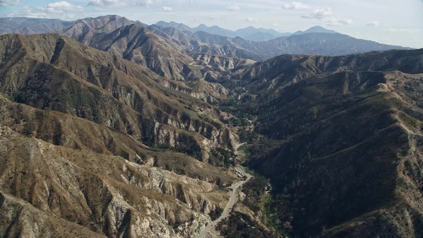Flying over a winding road in the canyons of Newhall California during a partly cloudy day with beautiful views of the surrounding nature and mountains