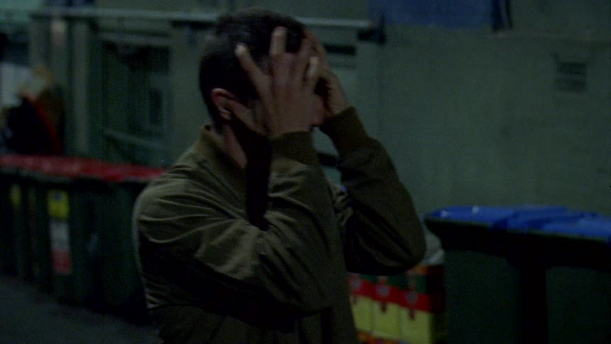A man smashing a skateboard off a wall in an alley and screaming into his hands in anger
