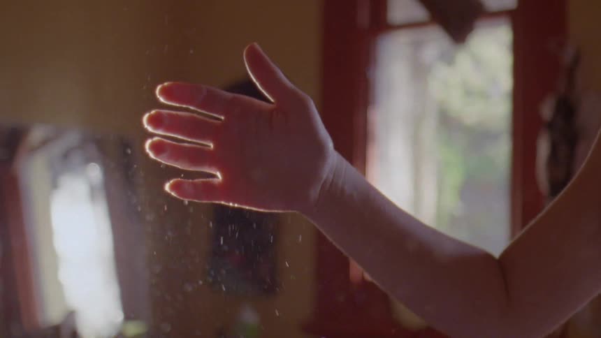 A woman holds her finger up in dust visible in sunlight in her home
