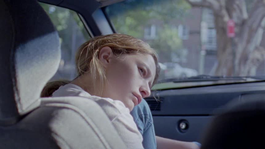 A sad woman hugs her knee while sitting in a parked vehicle