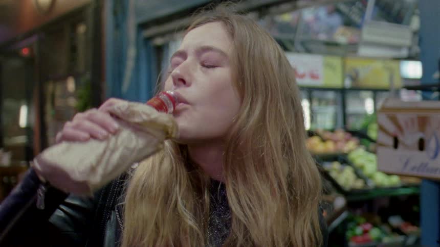 A man drinks alcohol out of a paper bag while standing at a grocery store