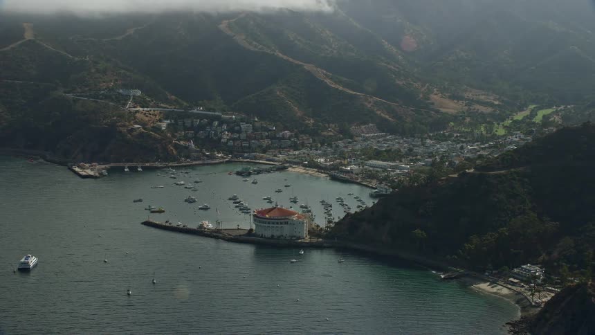 A stunning aerial view of Avalon Santa Catalina Island California with the town built into a cove in the ocean boats parked in the marina and surrounding mountains captured in epic helium shotover gear during spring or summer months