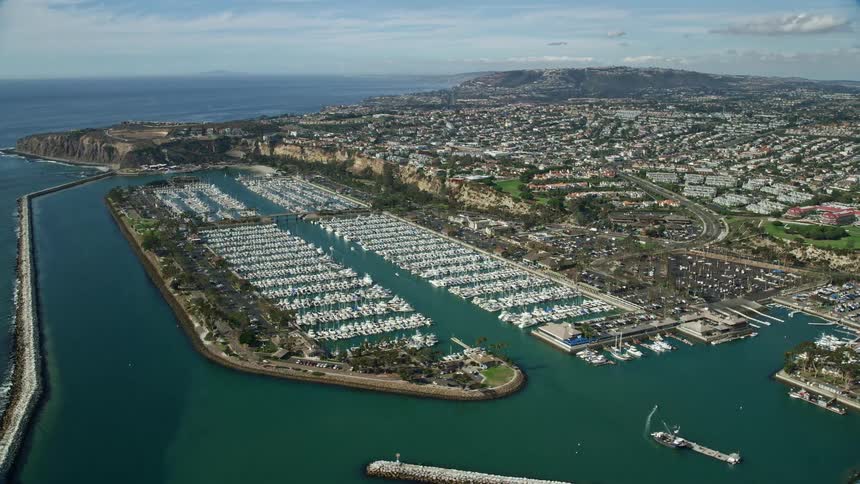 An aerial view of Dana Point Harbor and its surrounding seaside neighborhoods in southern California showcasing the docks boats and residential areas on a sunny day