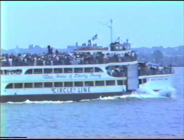 A ferry transports people across water with a pier in foreground with people standing and watching