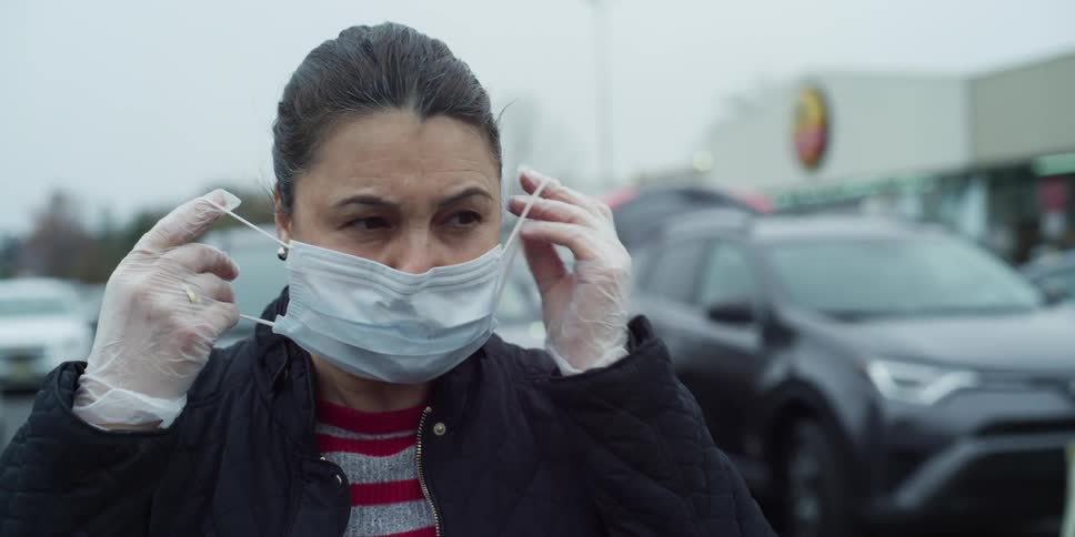 Woman putting on and taking off medical mask in parking lot of grocery store