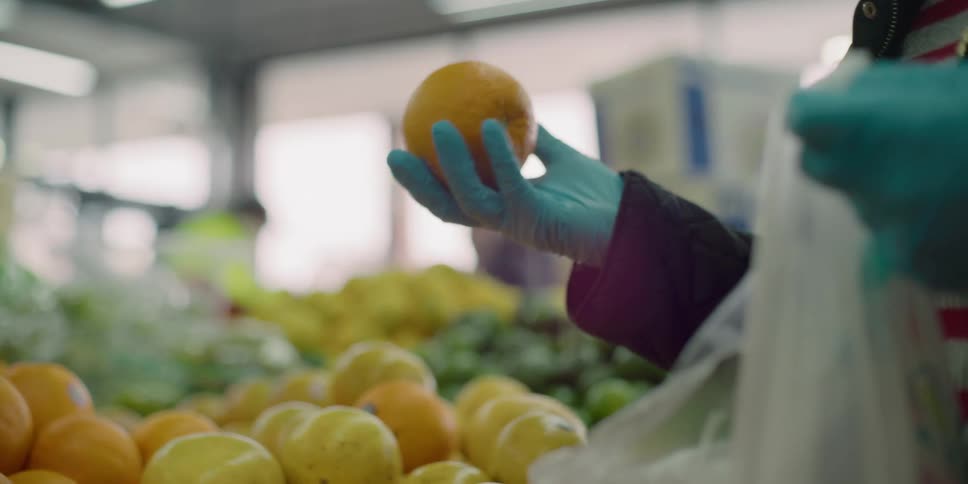 Woman wearing latex gloves buys fruit in supermarket