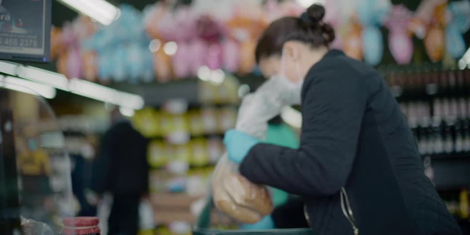 A woman in a grocery store with a mask taking groceries out of a shopping cart