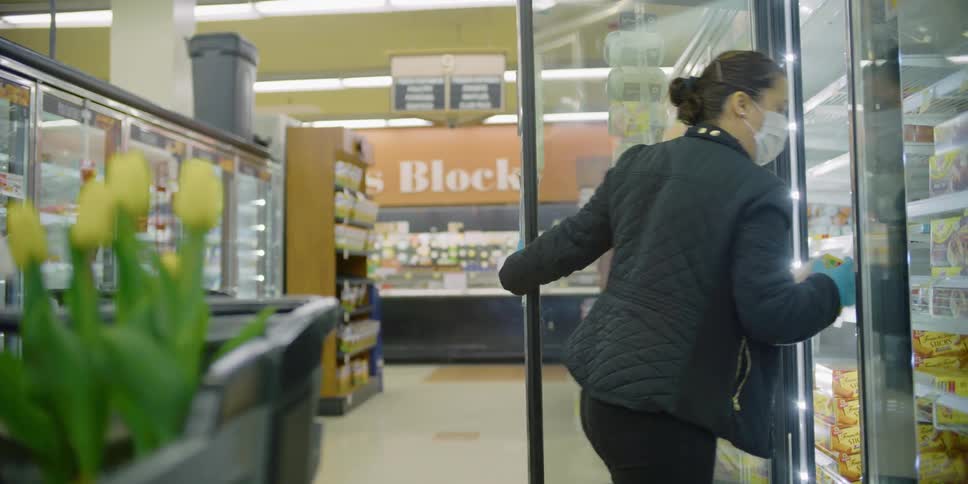 A woman wearing a mask gets waffles out of a freezer in a grocery store