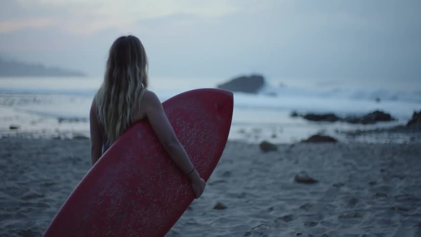 A woman carrying a surfboard to a beach