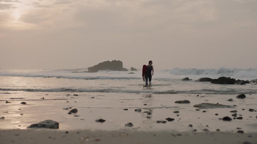A person is walking on the beach and holding their surf board