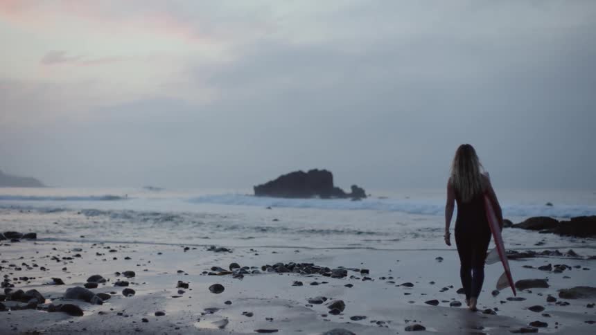 A woman is walking on the beach during sunset