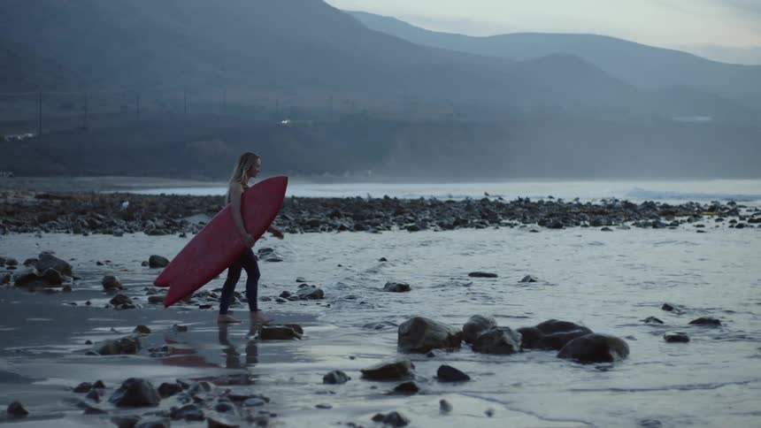 A young woman is walking with her surfboard around day time