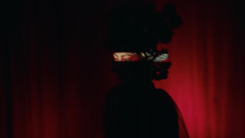 A woman in an elaborate asian headpiece and makeup starts to dance in front of a curtain as she goes from being a dark silhouette to full light