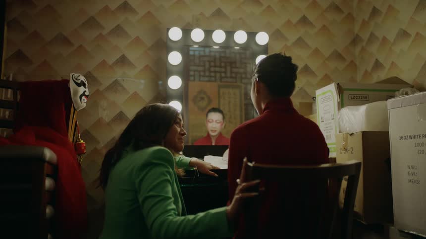 A woman in a green suit knelt down next to a woman sitting as they talk and smile and laugh