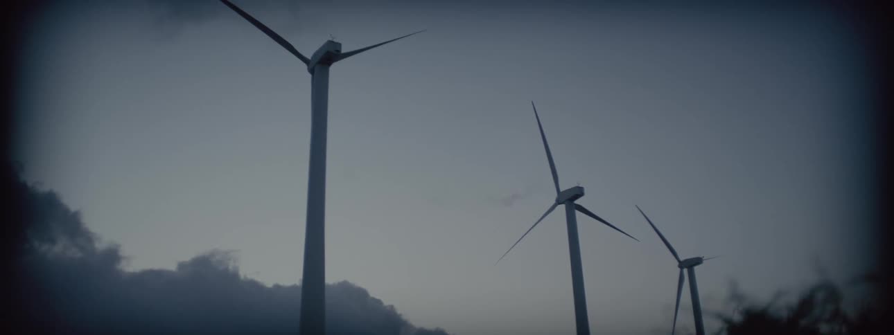 Three windmills turn slowly against a mostly clear sky with a hillside in the background