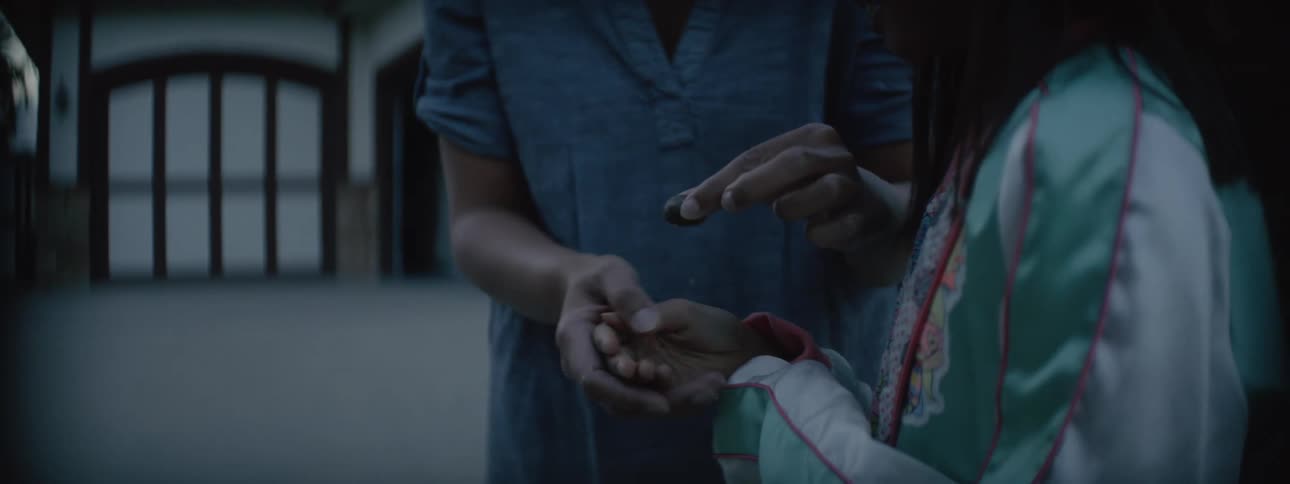 A mother and daughter standing outside as the mother places something dark and round into the girls hand