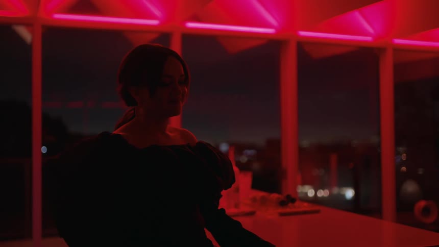 Woman wearing a black night dress pours a drink on the floor under red lights