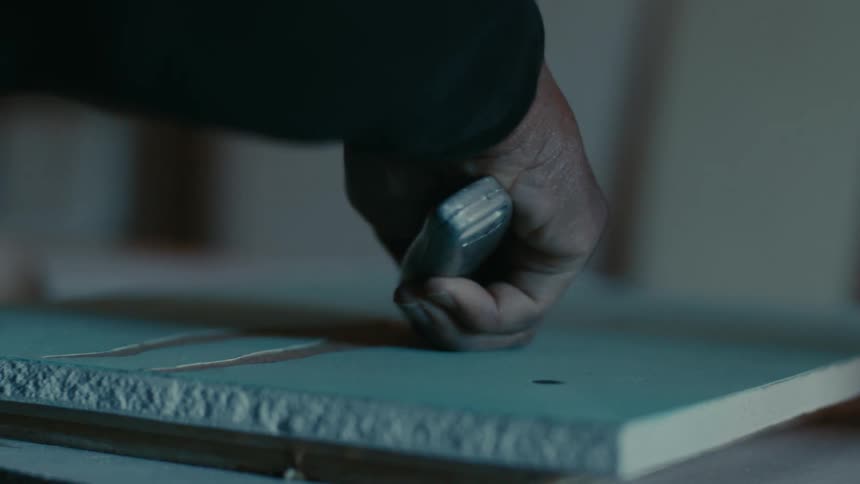 Close up of the hands of a carpenter carving a piece of wood with a knife