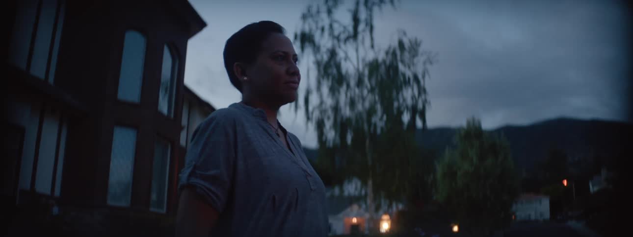 An adult woman standing outside her home looking into the distance at dusk